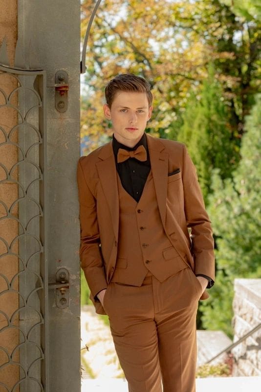 A man in brown suit standing next to a wall.