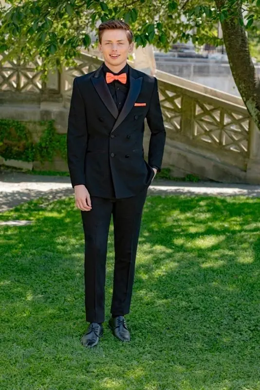 A man in a suit and bow tie standing on the grass.